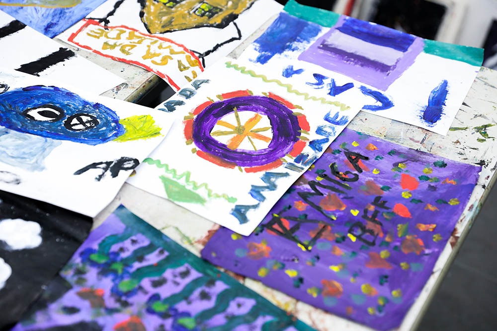 Em cima de uma mesa estão várias pinturas feitas pelas crianças do projeto incluarte.