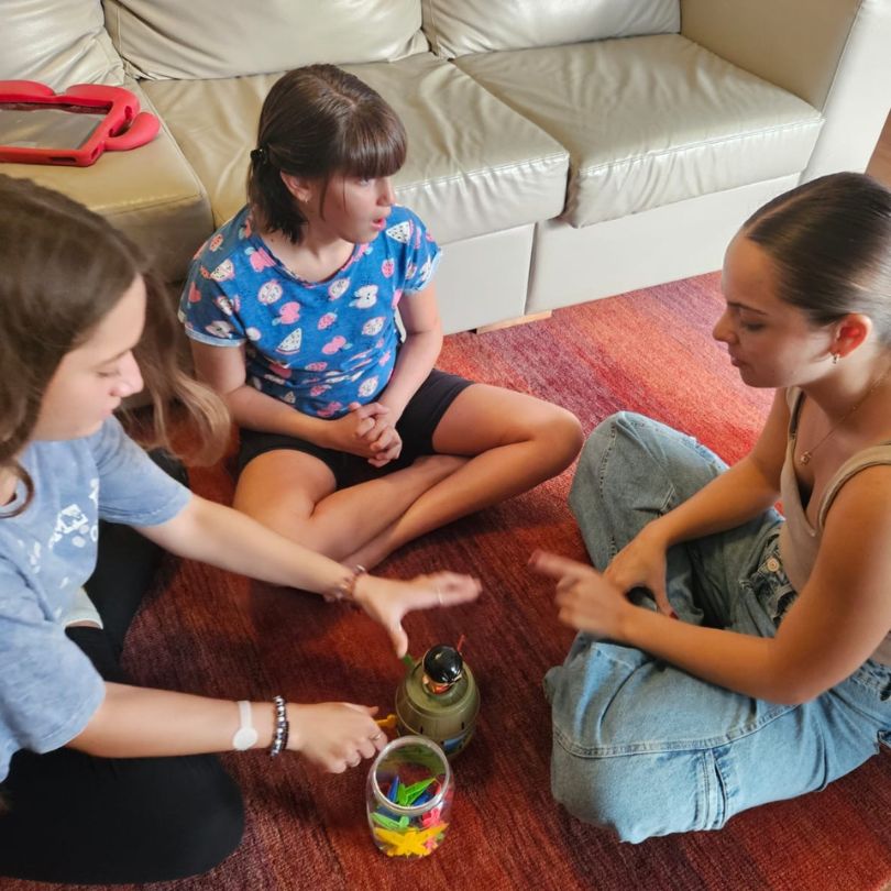 Três meninas sentadas no chão, brincando alegremente com brinquedos coloridos ao seu redor.