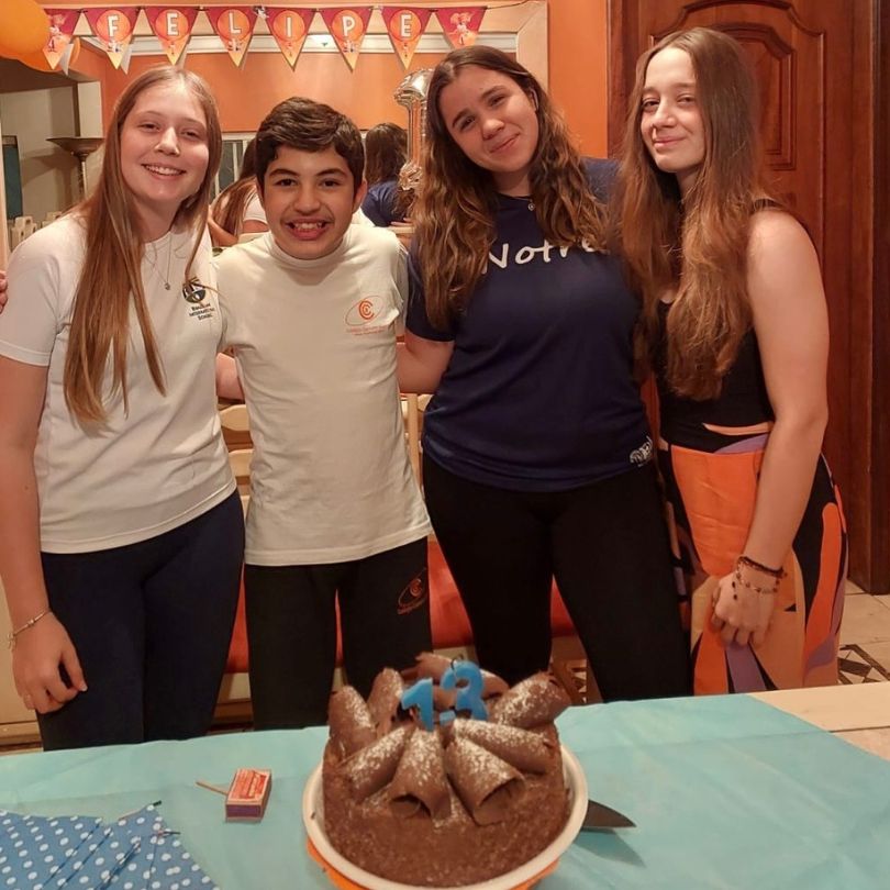 Três meninas e um menino posam para uma foto em frente a um bolo decorado.