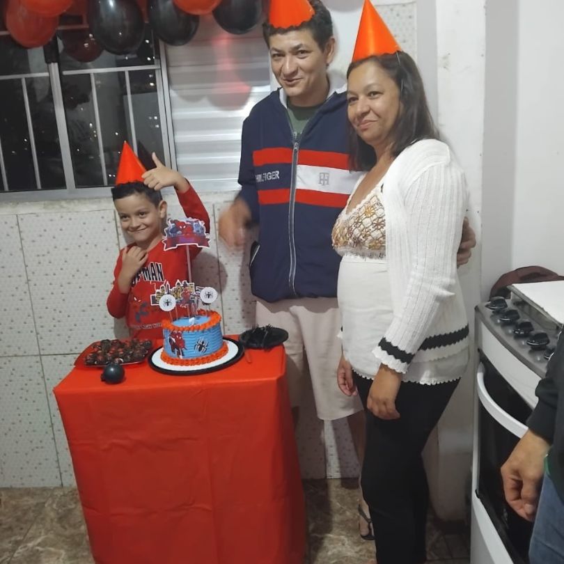 Uma família sorridente posa para uma foto ao lado de um bolo de aniversário decorado.