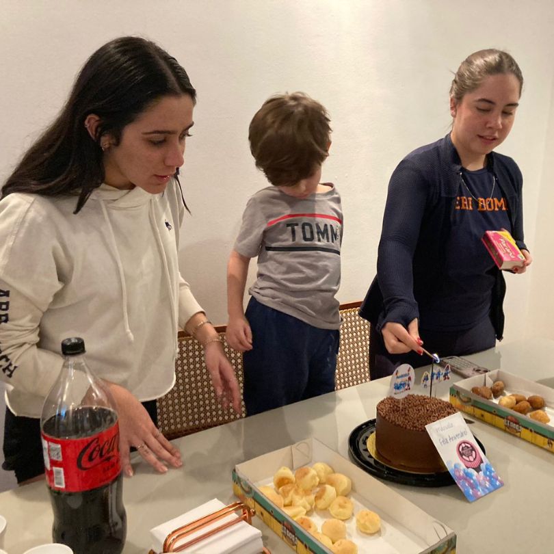 Duas jovens e uma crianças ao redor de uma mesa com um bolo, celebrando um momento especial.