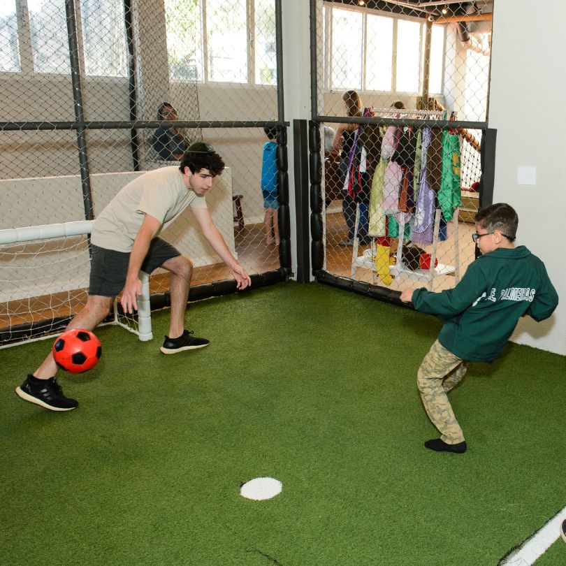 Homem e menino jogando futebol em um ambiente interno, demonstrando alegria e interação entre eles.