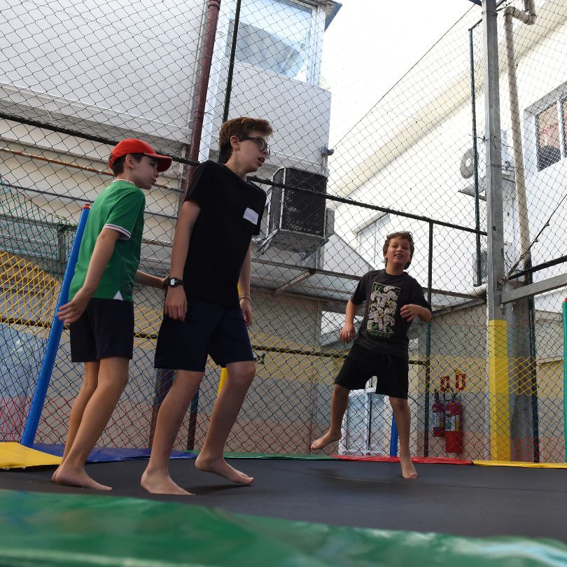 Três meninos se divertindo em um trampolim no quintal, saltando e rindo juntos em um dia ensolarado.